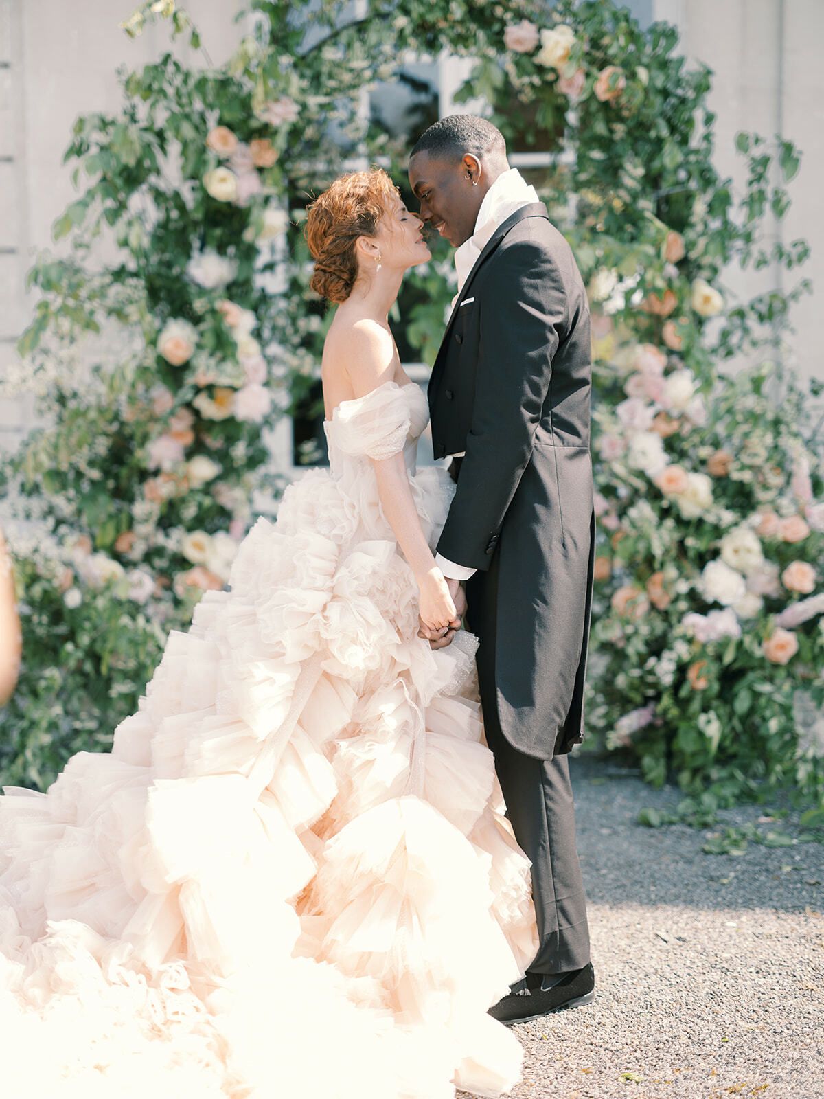 Novia con vestido de volantes besando al novio bajo un arco floral