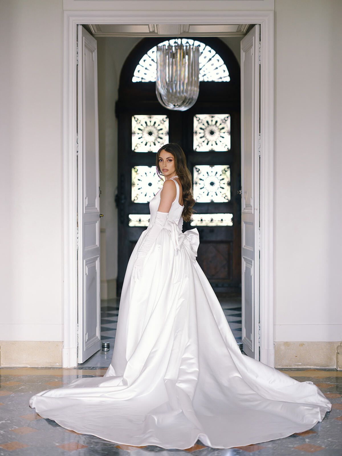 Novia con vestido de satén de larga cola enmarcada por una puerta del château