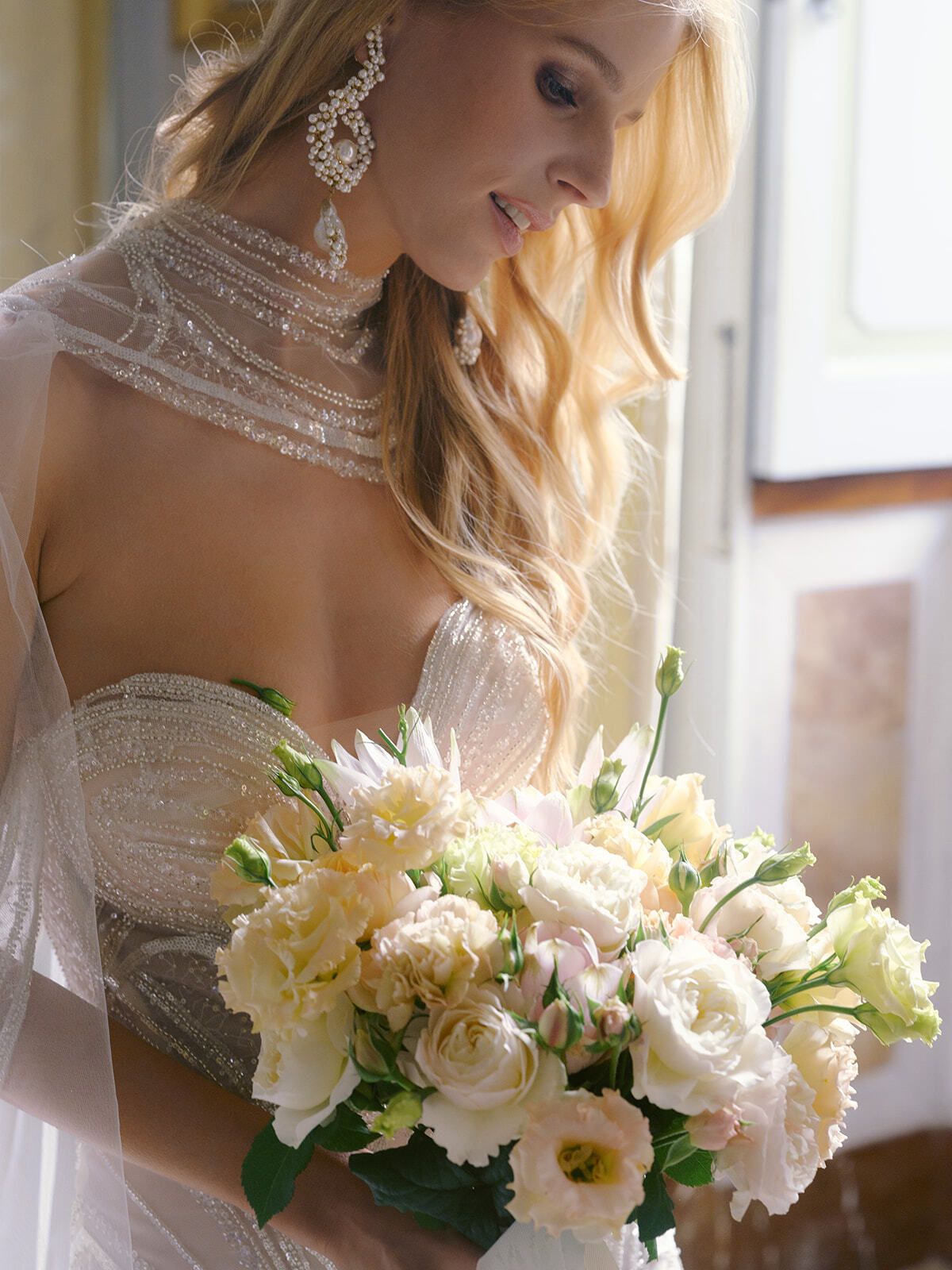 Mariée en robe ornée de cristaux tenant des roses blanches