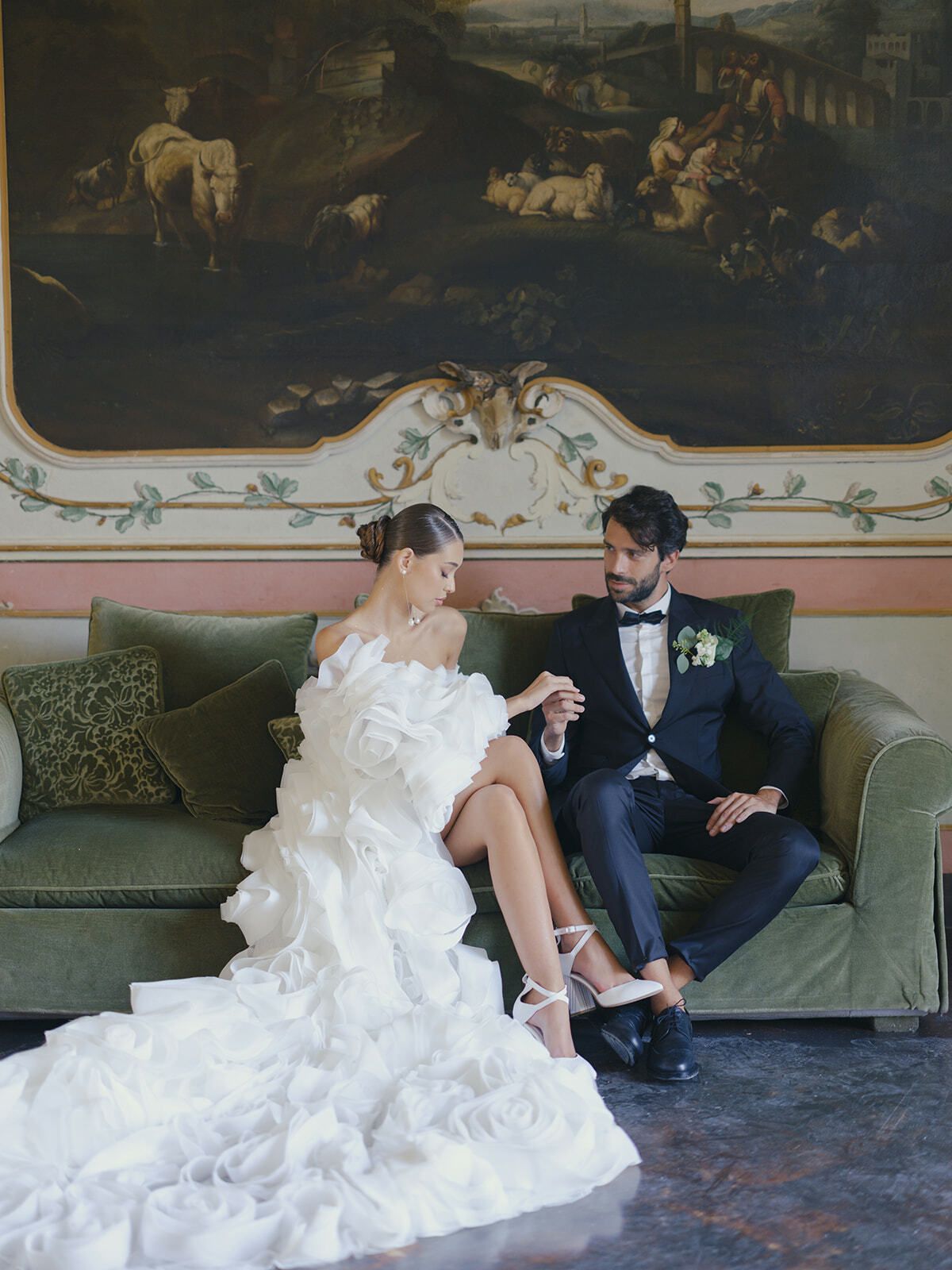 Braut im Rüschenkleid mit dem Bräutigam auf einem grünen Sofa unter einem alten Gemälde