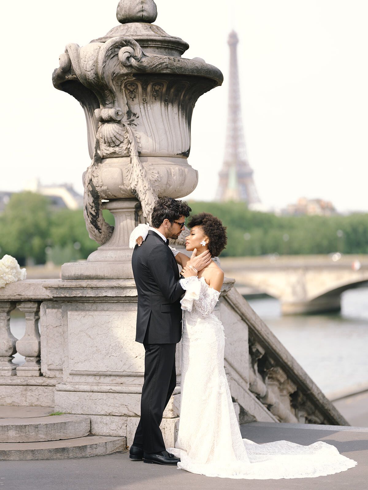 Couple by an ornate lamp on Pont Alexandre III with the Eiffel Tower behind