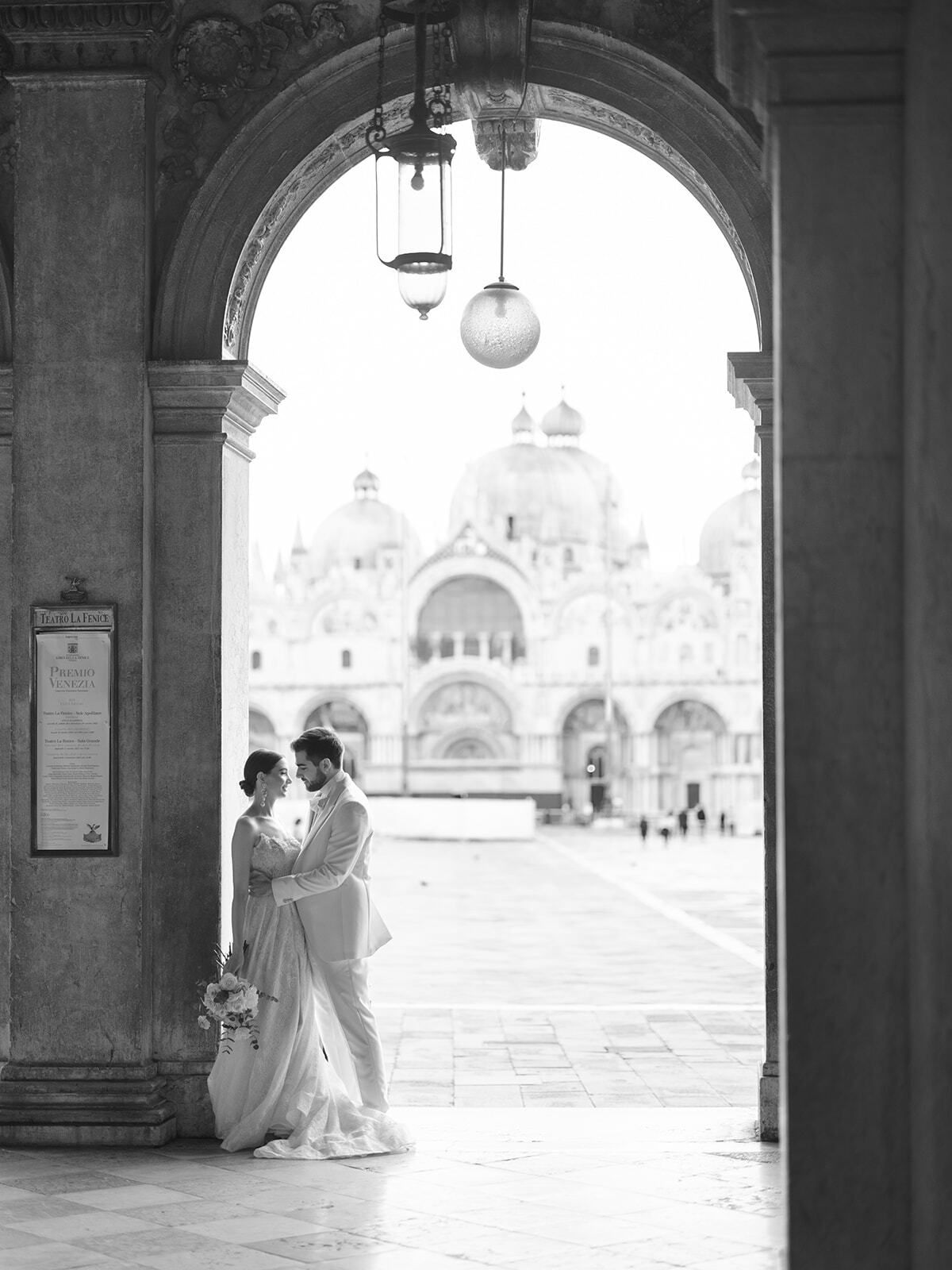 Foto in bianco e nero di una coppia incorniciata da un arco di fronte alla Basilica di San Marco