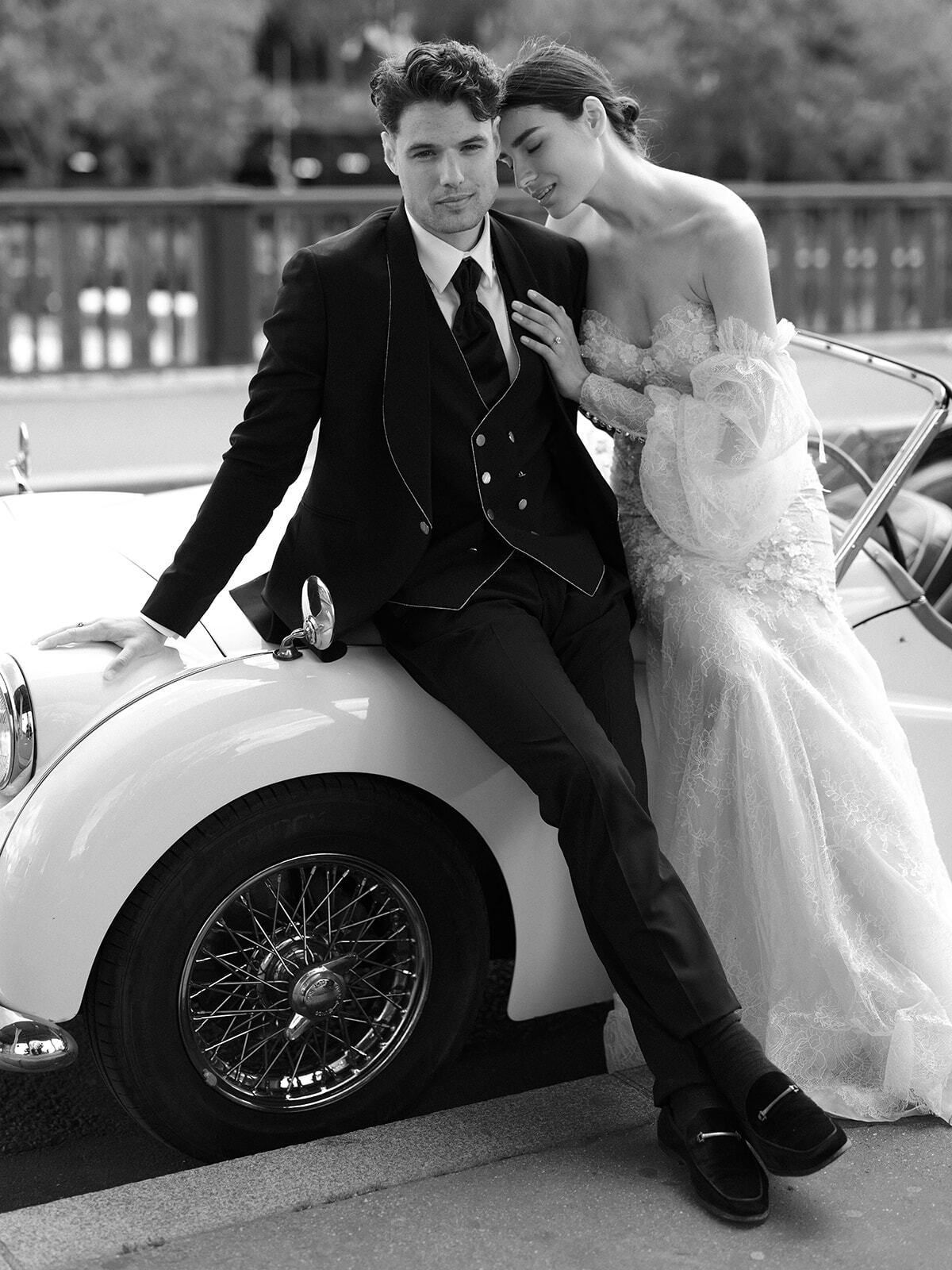 Foto en blanco y negro de una pareja apoyada en un roadster clásico