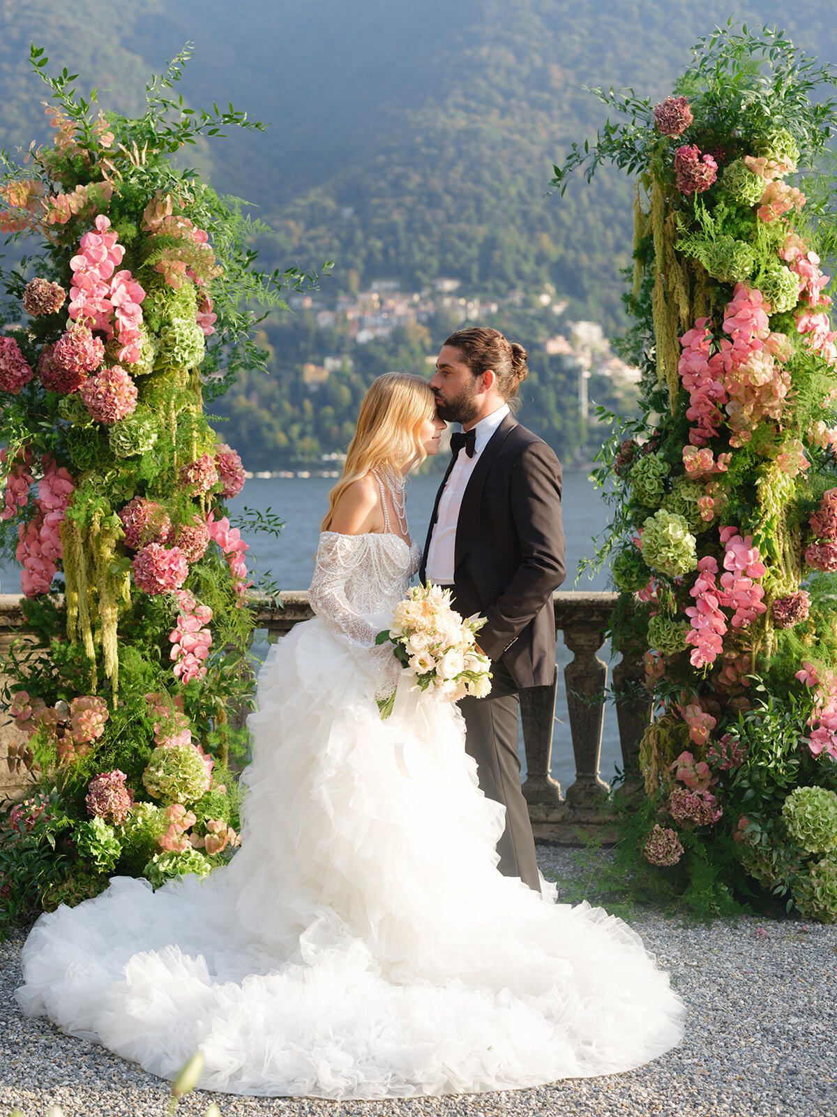 Bride in a ruffled gown with the groom under floral arches, Lake Como