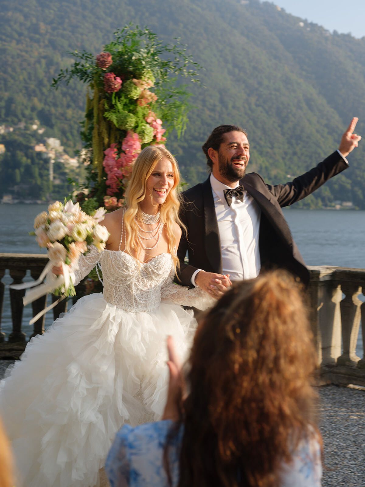 Groom cheering beside the bride under the floral arch, Lake Como