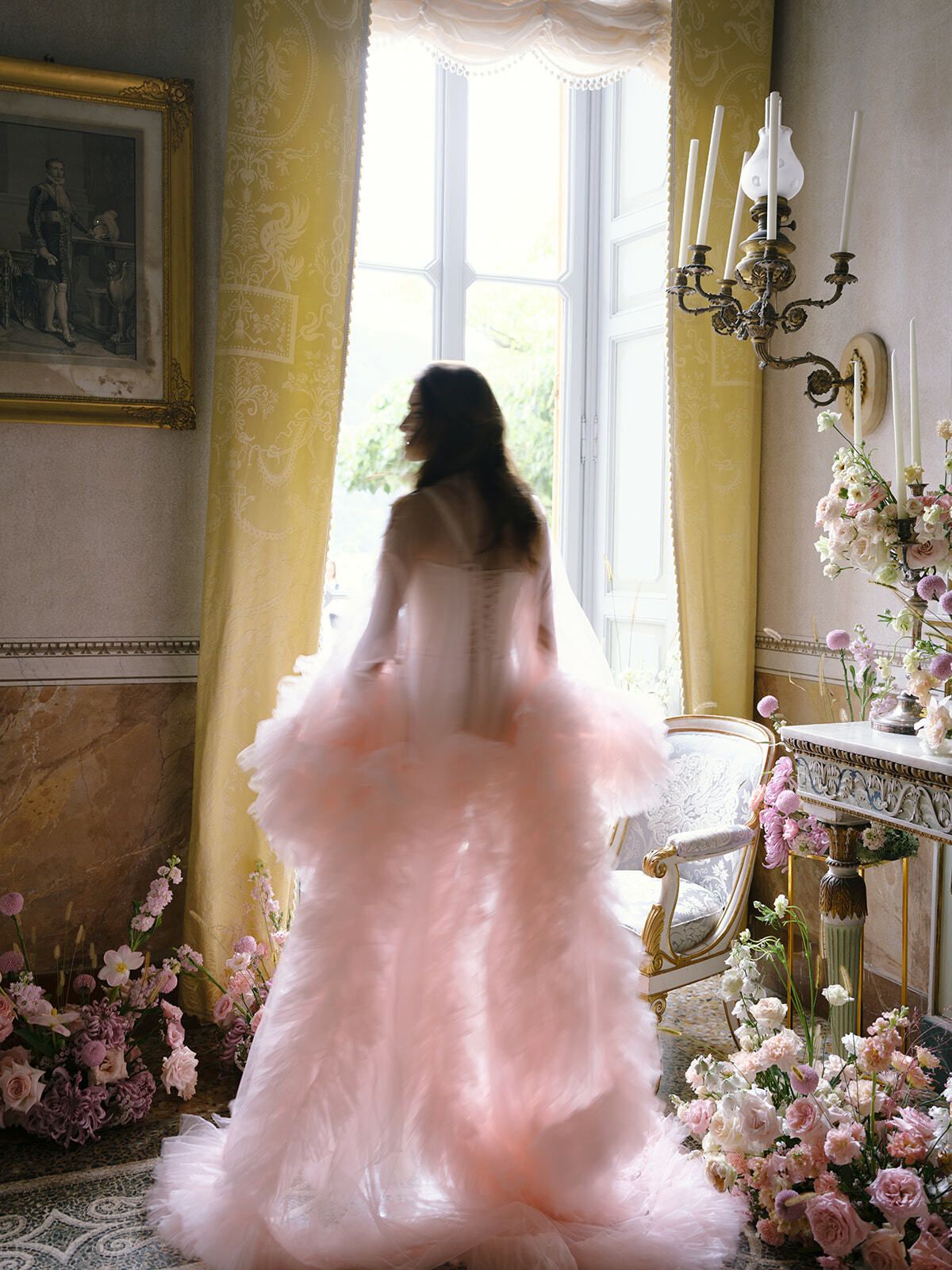 Novia con bata de volantes rosa junto a una ventana soleada