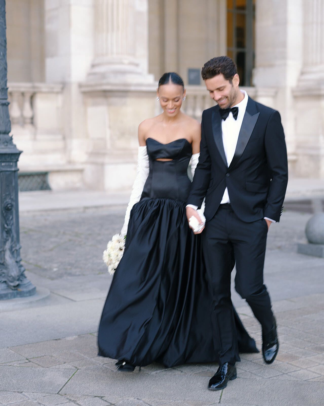 Paar in Schwarz geht Hand in Hand am Louvre