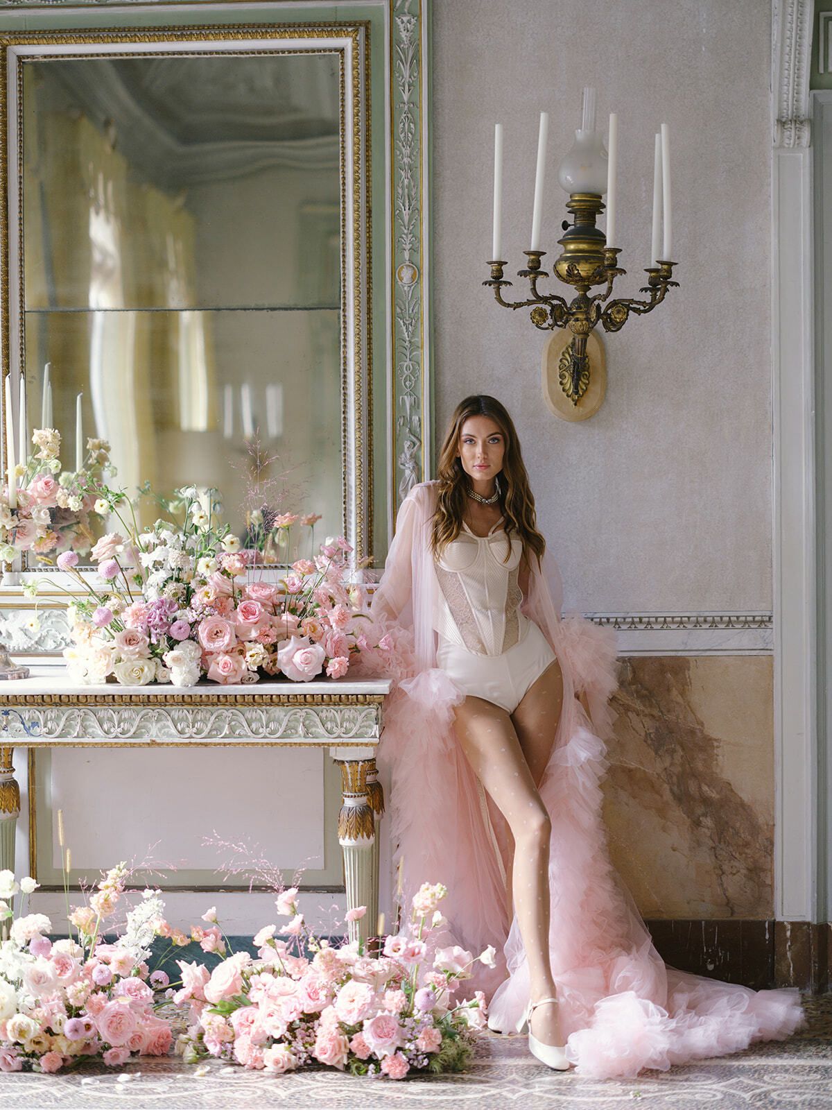 Novia con una bata rosa transparente en un salón lleno de flores