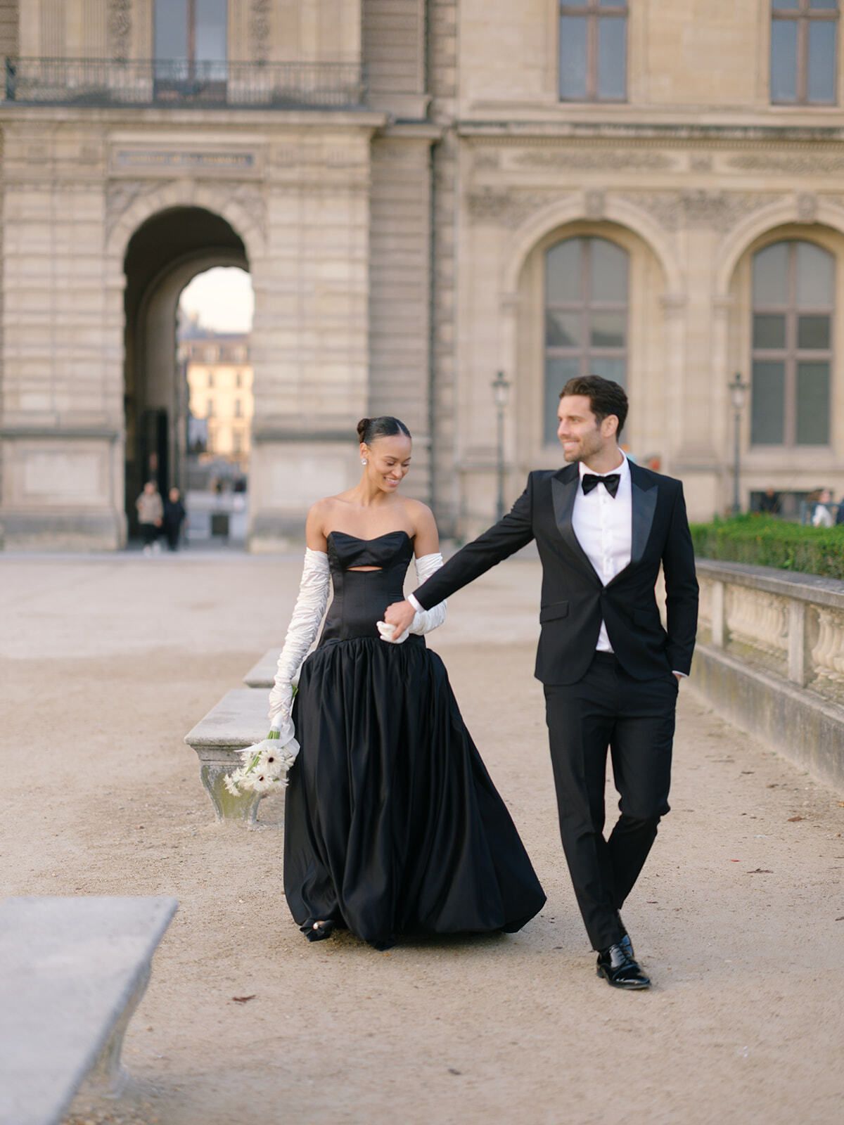 Paar in Schwarz spaziert durch den Hof des Louvre