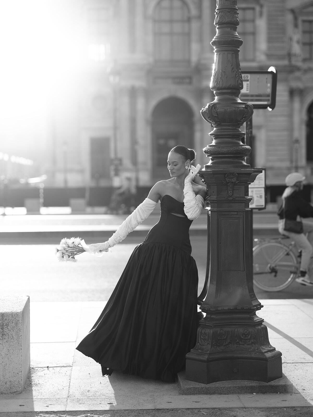 Schwarz-Weiß-Foto einer Frau im schwarzen Kleid an einer Laterne, Paris