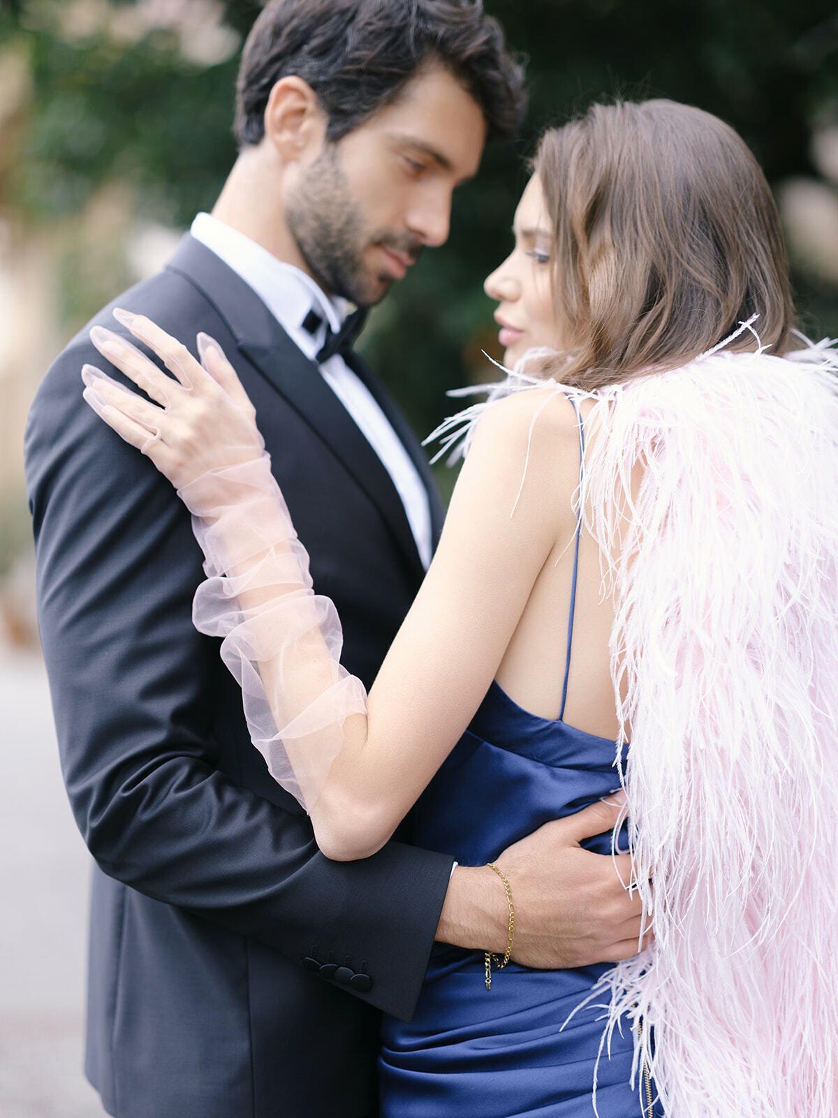 Invitada con abrigo de plumas rosa abrazando a un hombre de esmoquin