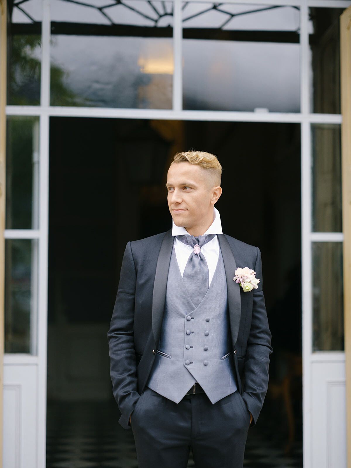 Novio con chaleco gris y traje azul marino en la puerta de una villa