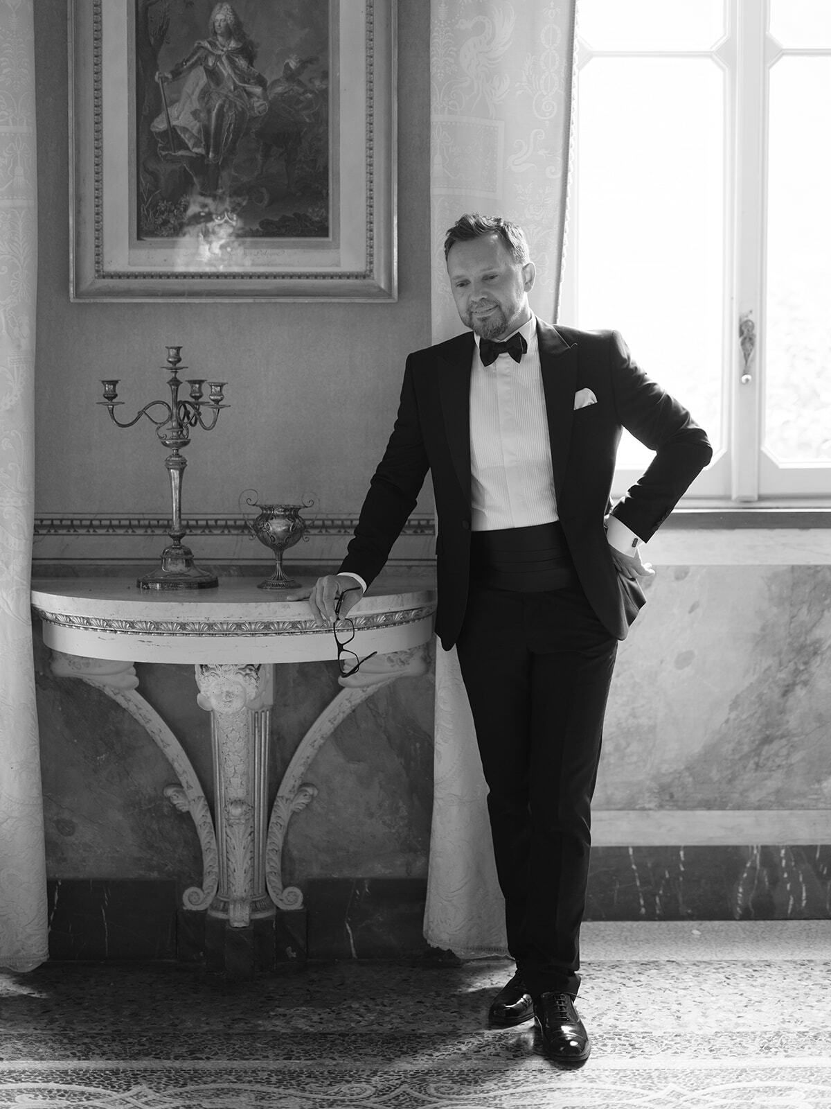 Retrato en blanco y negro de un novio de esmoquin en un salón de la villa