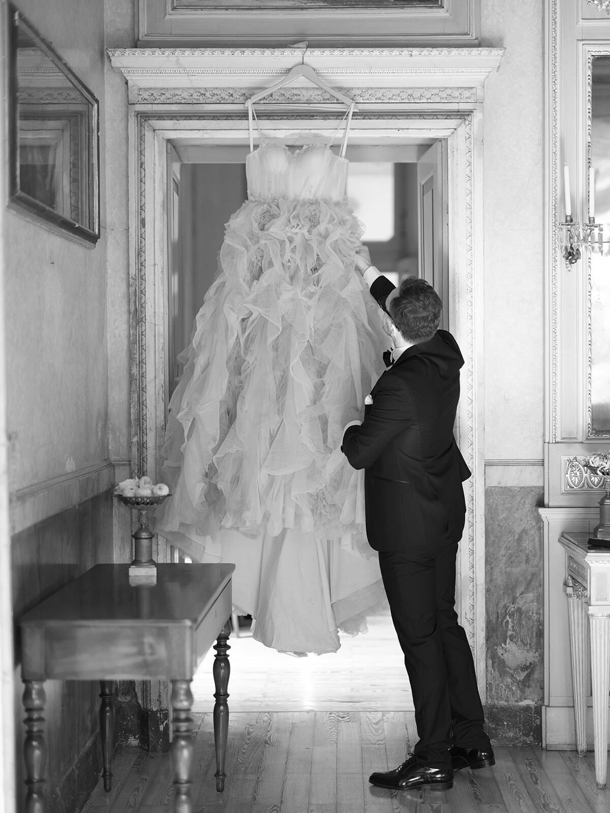 Foto en blanco y negro del novio mirando el vestido de novia colgado