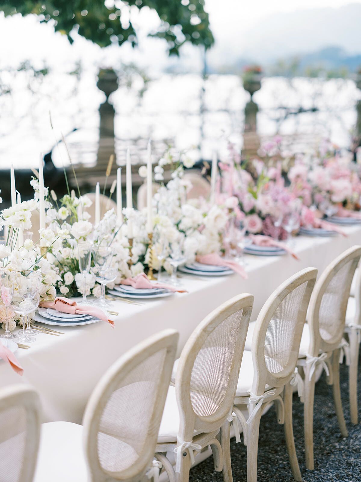 Mesa larga de banquete con flores rosas y sillas de mimbre junto al lago