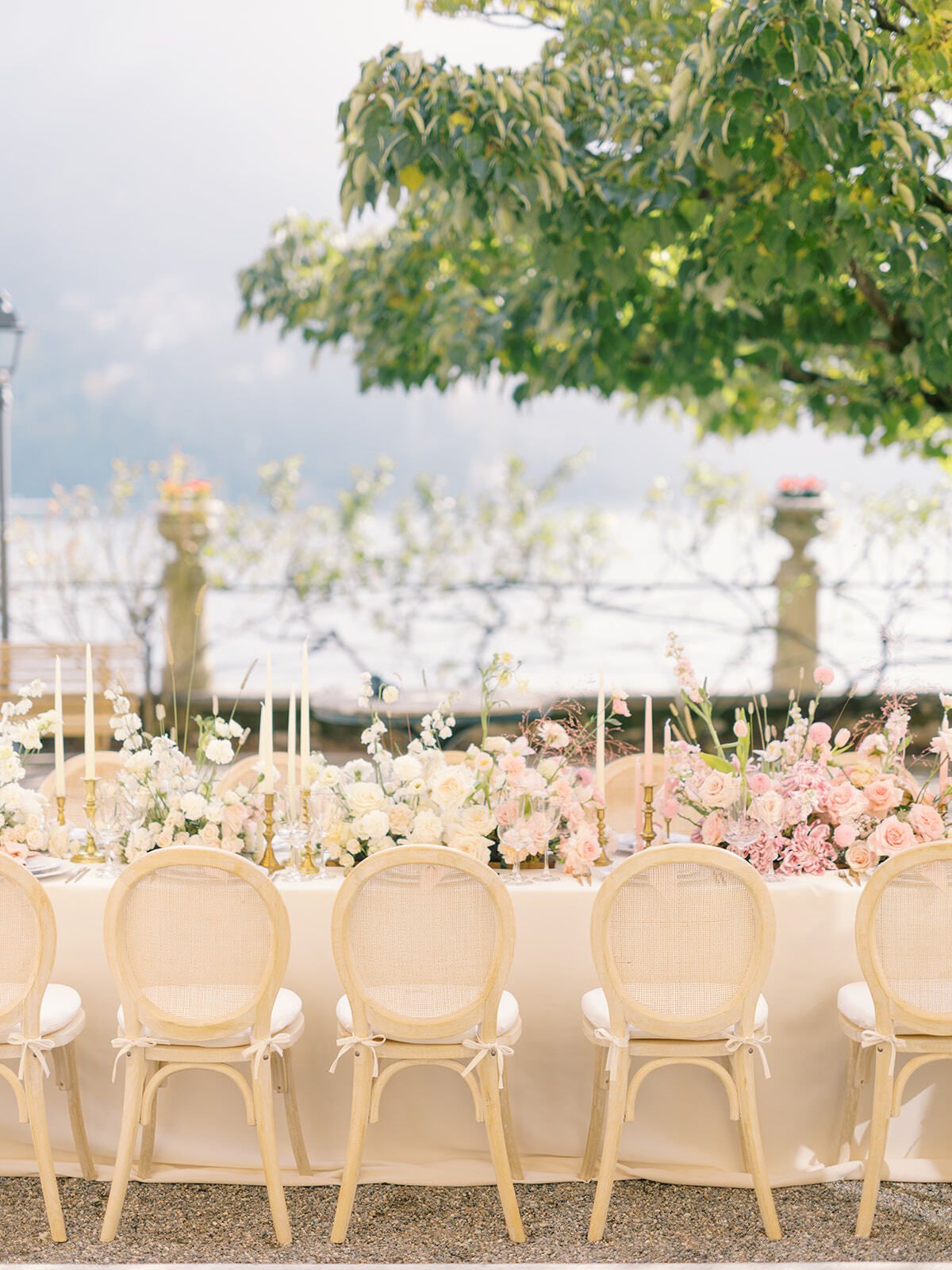 Larga mesa de banquete con flores rosas en la terraza junto al lago