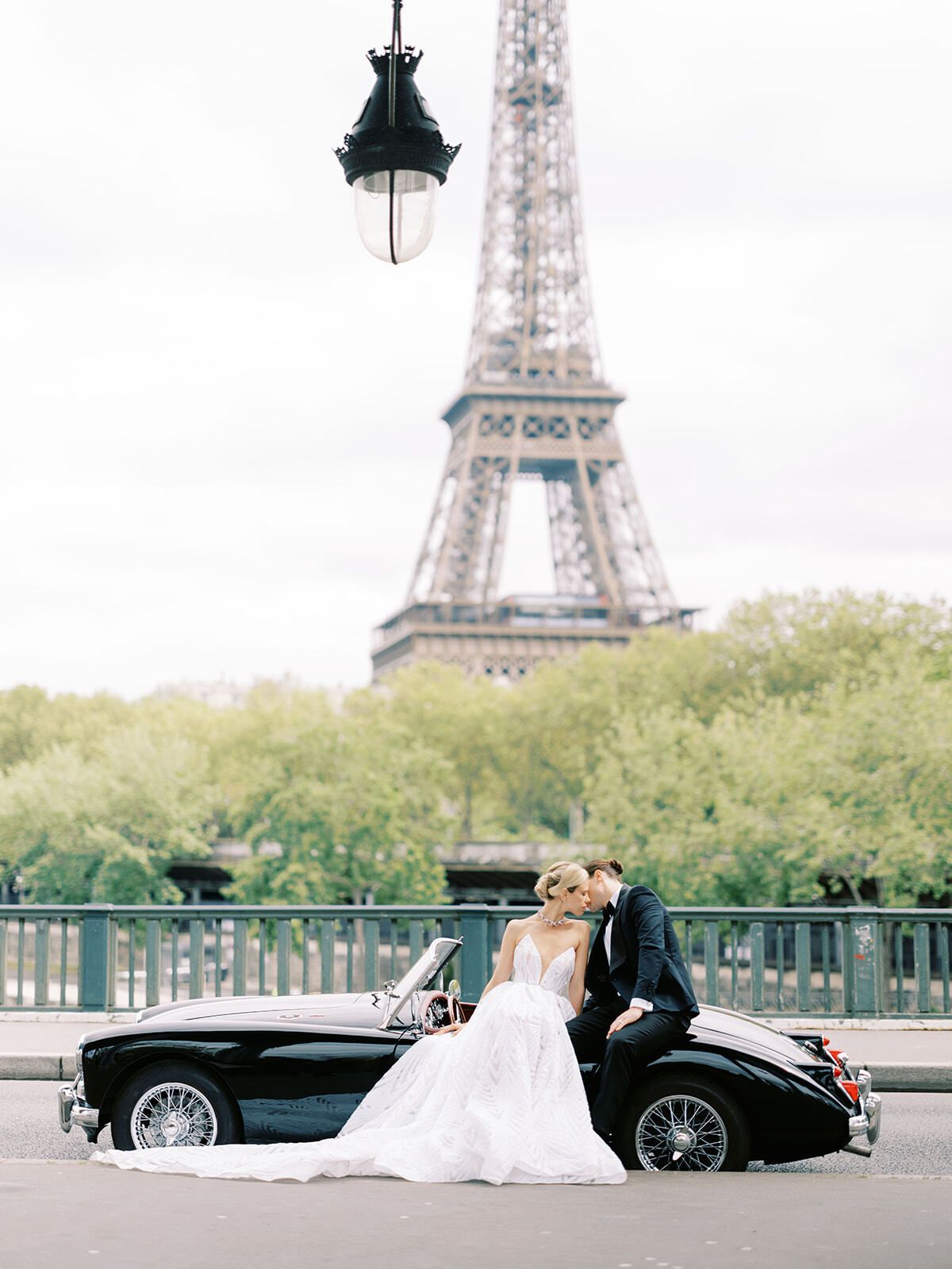 Mariés s’embrassant près d’un cabriolet ancien devant la tour Eiffel, Paris